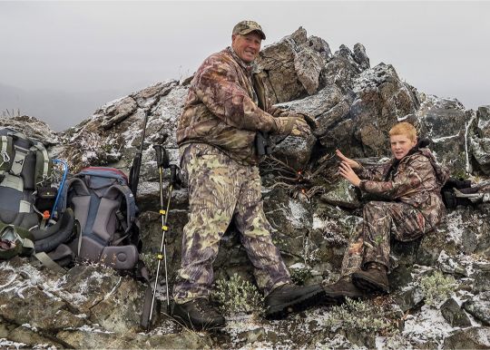 Family affair: Grandfather and a grandson enjoy a small warming fire and lunch on a rocky ridgeline while looking for mule deer in the basin below.